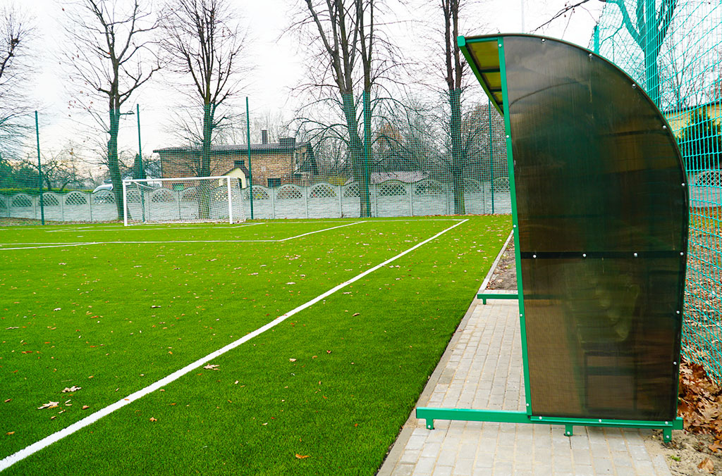 Boisko do piłki nożnej typu Orlik, wzdłuż boiska zadaszone siedziska sportoweaszone