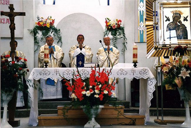 Ołtarz w kościele, przed nim kwiaty, przy ołtarzu mszę świętą sprawuje czterech księży