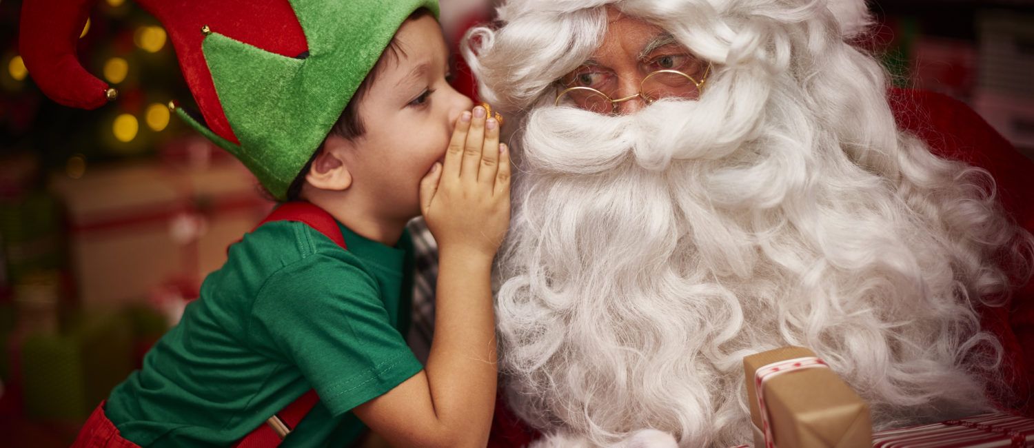 Chłopczyk w stroju elfa szepcze mikołajowi do ucha