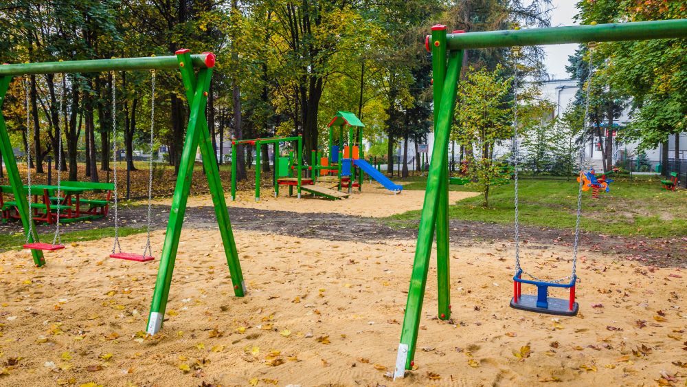 Plac zabaw w parku na nim huśtawki dla dzieci w tle zestaw zabawowy