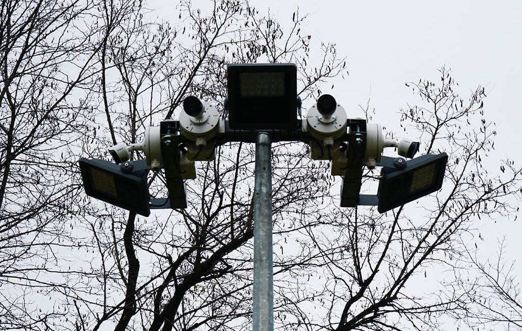 Słup oświetleniowy i kamery monitoringu, w tle drzewa