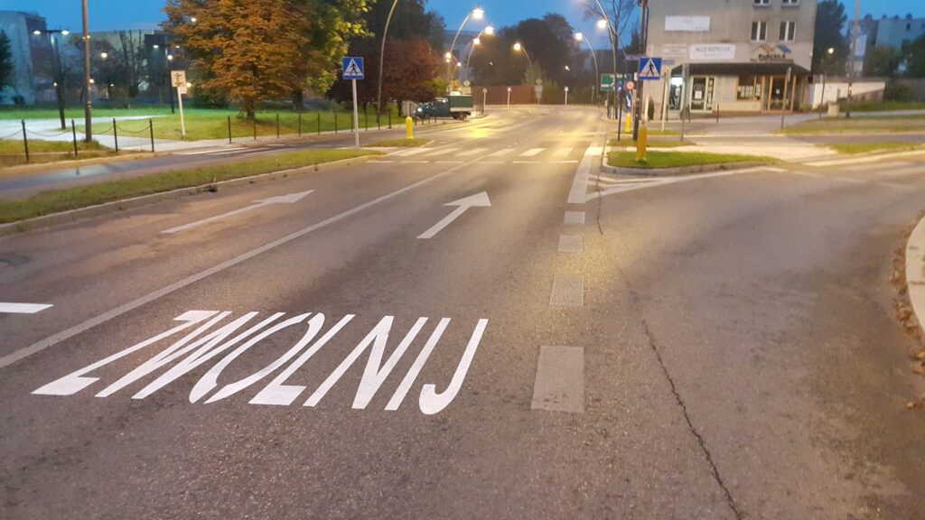 Jezdnia, a na niej namalowany napis przed przejściem dla pieszych o treści zwolnij