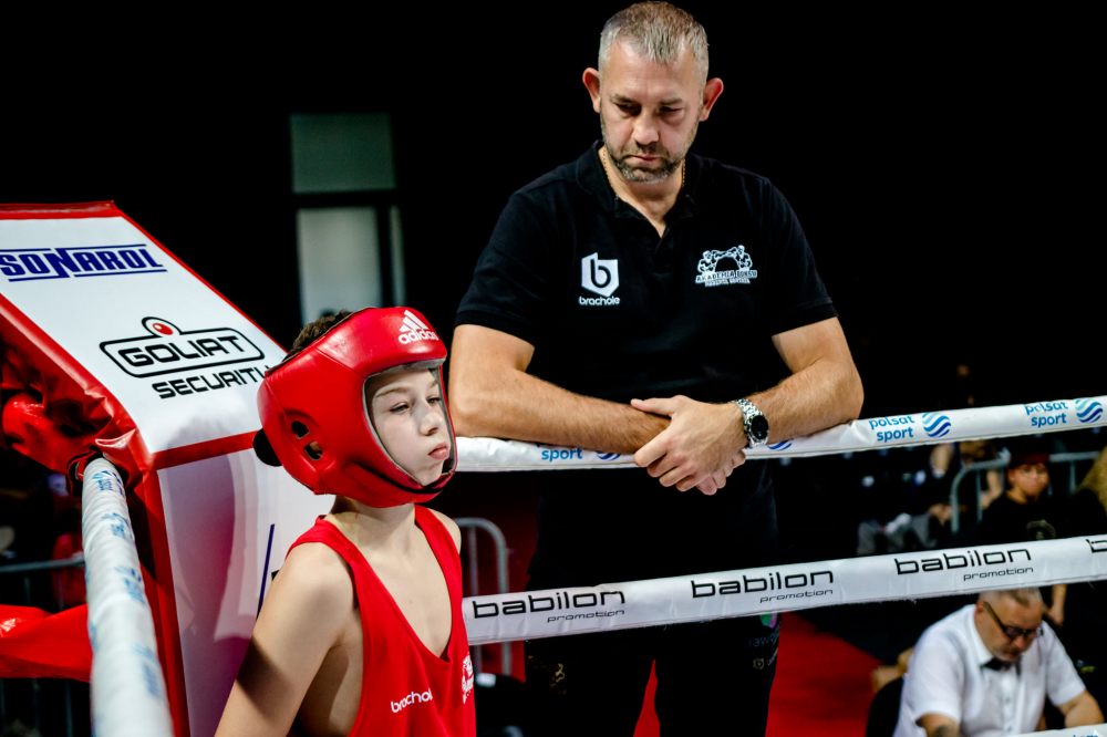Dziecko - bokser na ringu, na wprost przygląda mu się trener
