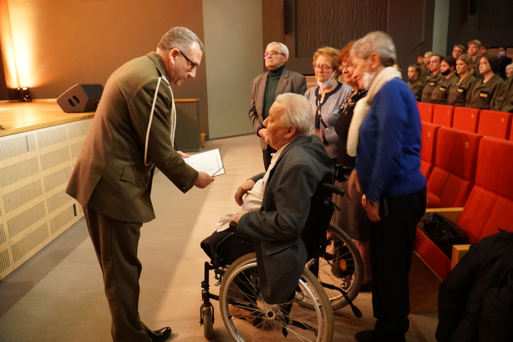 Żołnierz wręczający mężczyźnie na wózku inwalidzkim list, w tle grupa osób