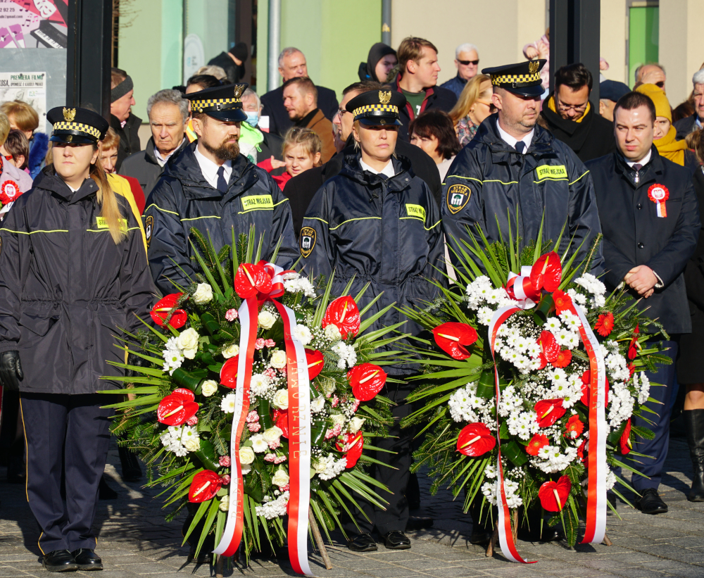 Czterech strażników miejskich w umundurowaniu trzymających dwa biało-czerwone wieńce