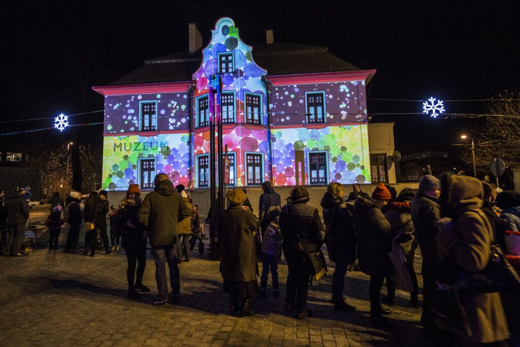 Grupa ludzi oglądająca budynek, na którym wyświetlają się świąteczne iluminacje