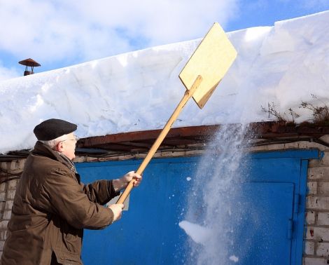 Mężczyzna ściągający za pomocą łopaty śnieg z dachu