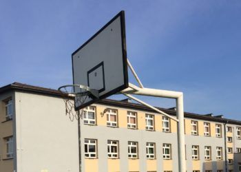 Obręcz i tablica do gry w koszykówkę, w tle budynek szkoły