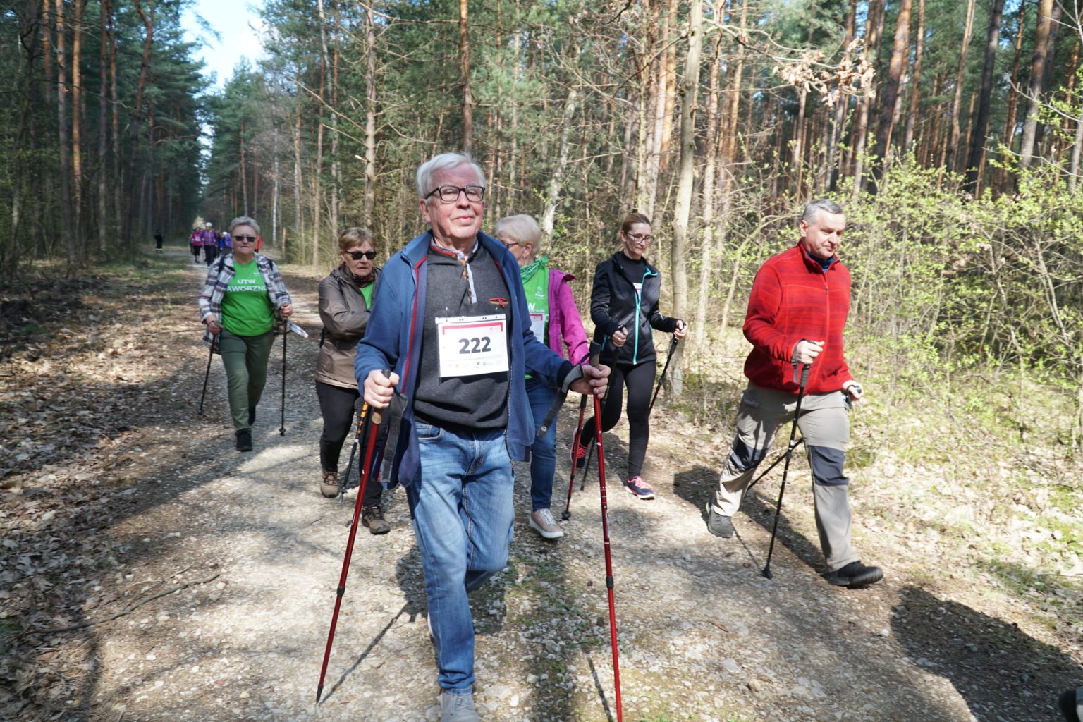 Grupa osób na trasie nordic walking prowadzącej przez las