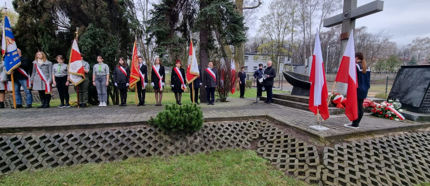Grupa ludzi z kwiatami pod pomnikiem poległych kolejarzy w Jaworznie Szczakowej