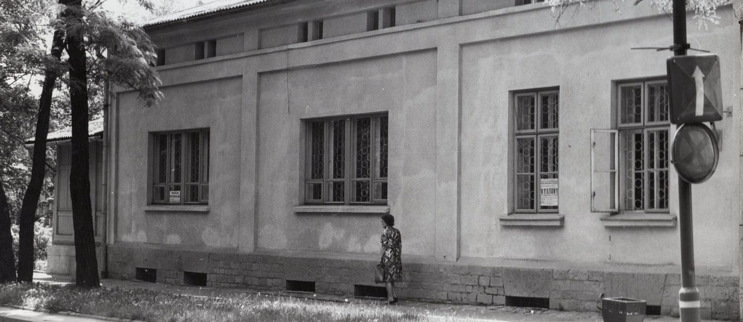 Czarno-białe zdjęcie budynku, przed budynkiem spaceruje kobieta