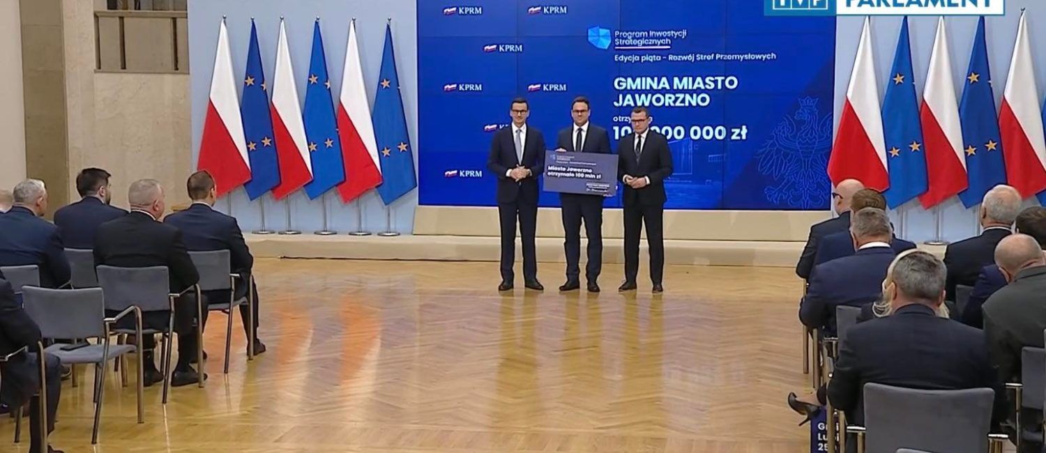 Trzech mężczyzn pozujących do zdjęcia, po lewej flagi Polski i Unii Europejskiej