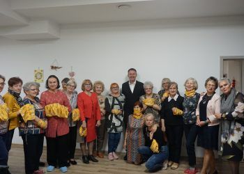Grupa osób pozująca do zdjęcia, część trzma w rękach żółte tkaniny