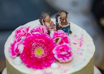 Biały tort z różowymi kwiatami oraz figurkami babci i dziadka.