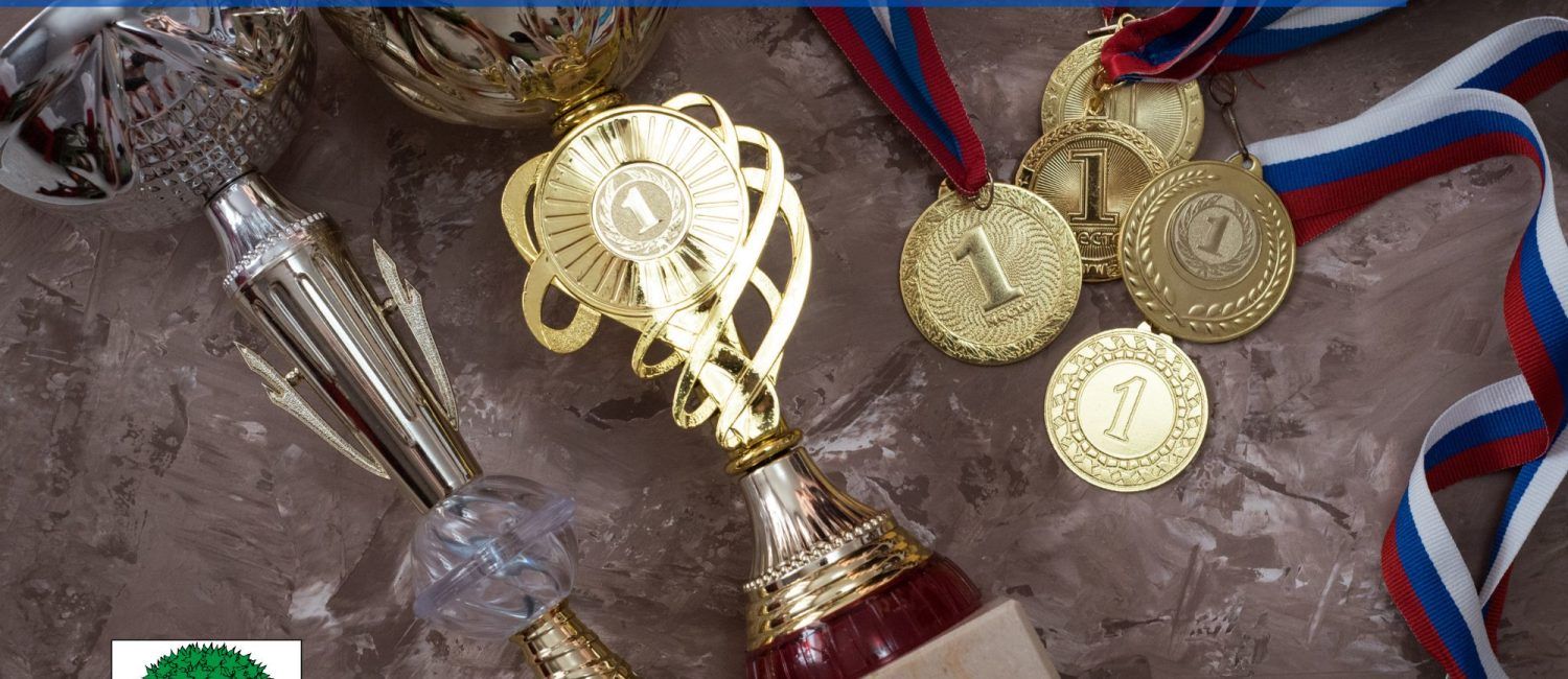 Zdjęcie medali oraz pucharów z herbem miasta, i paskami z napisem: Nagrody Sportowe Miasta Jaworzna i Jaworzno Bez Przerwy